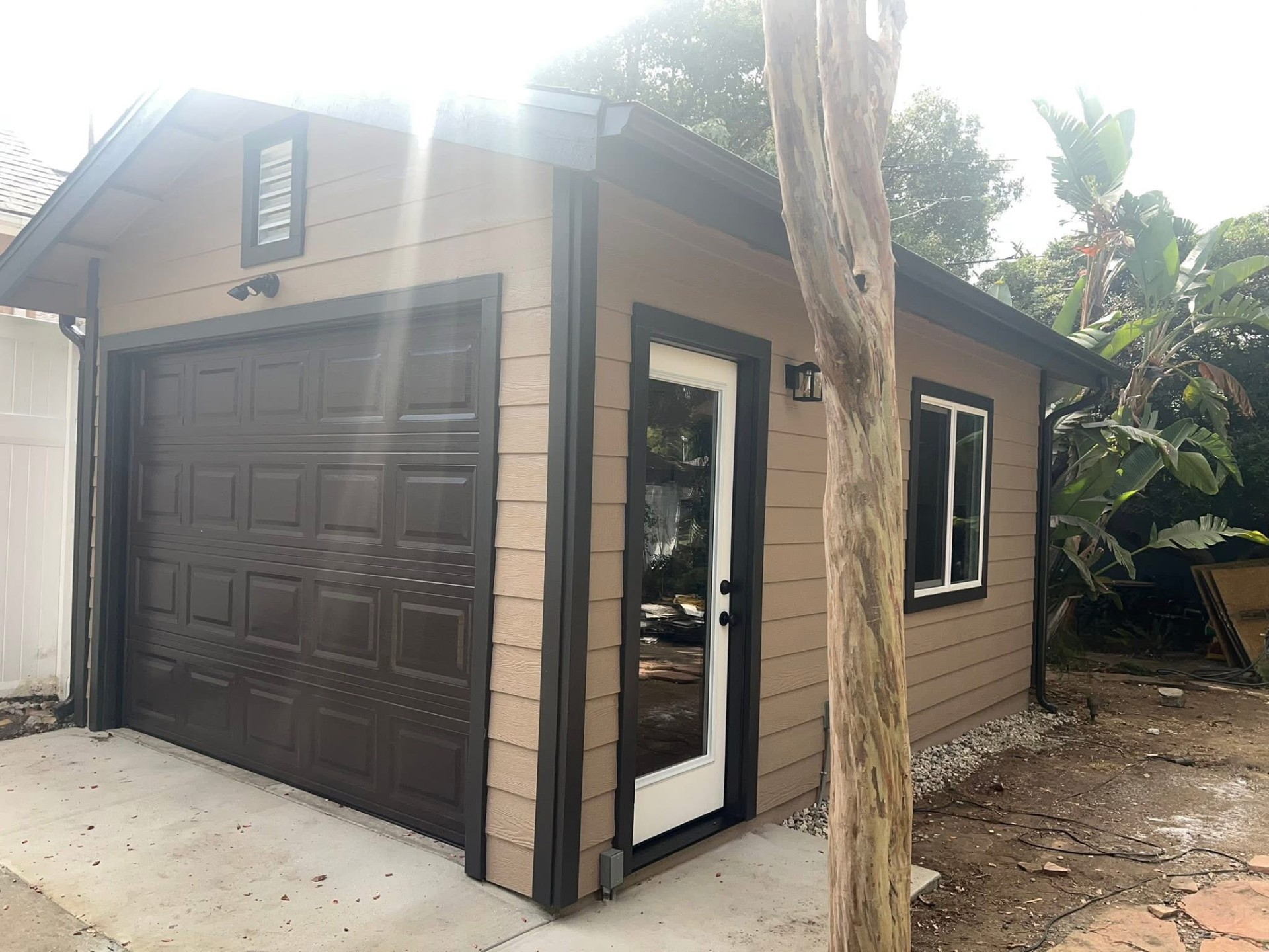 Newly built single-car detached garage with dark trim, side entry door, and fresh siding
